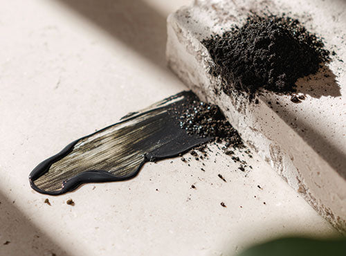 Ciemny proszek i rozsmarowana masa mumio na jasnym kamiennym blacie w naturalnym świetle.