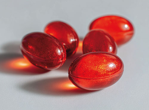 Pięć czerwonych kapsułek oleju z kryla ułożonych na jasnej powierzchni.