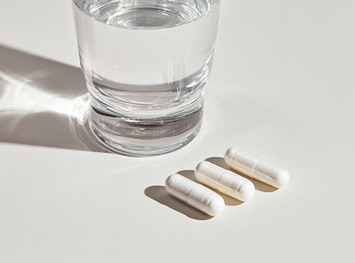 Szklanka wody i trzy kapsułki suplementu Potas Forte Biowen na jasnym tle.