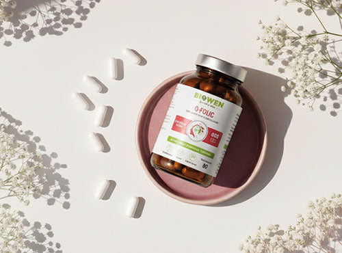 Suplement Q-folic Kwas Foliowy Biowen 90 kapsułek na różowym talerzyku z rozłożonymi kapsułkami na stole.