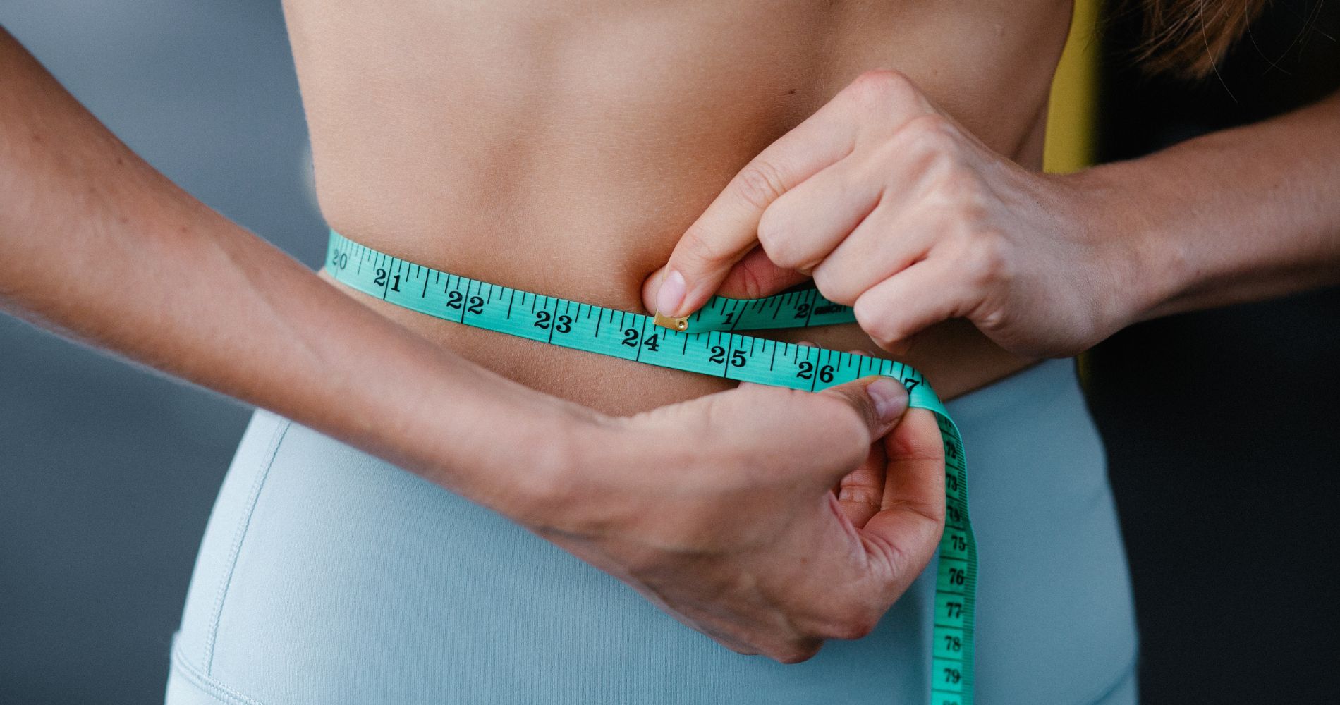 Jak przyspieszyć metabolizm – kobieta mierzy obwód talii jako element kontroli sylwetki i przemiany materii.