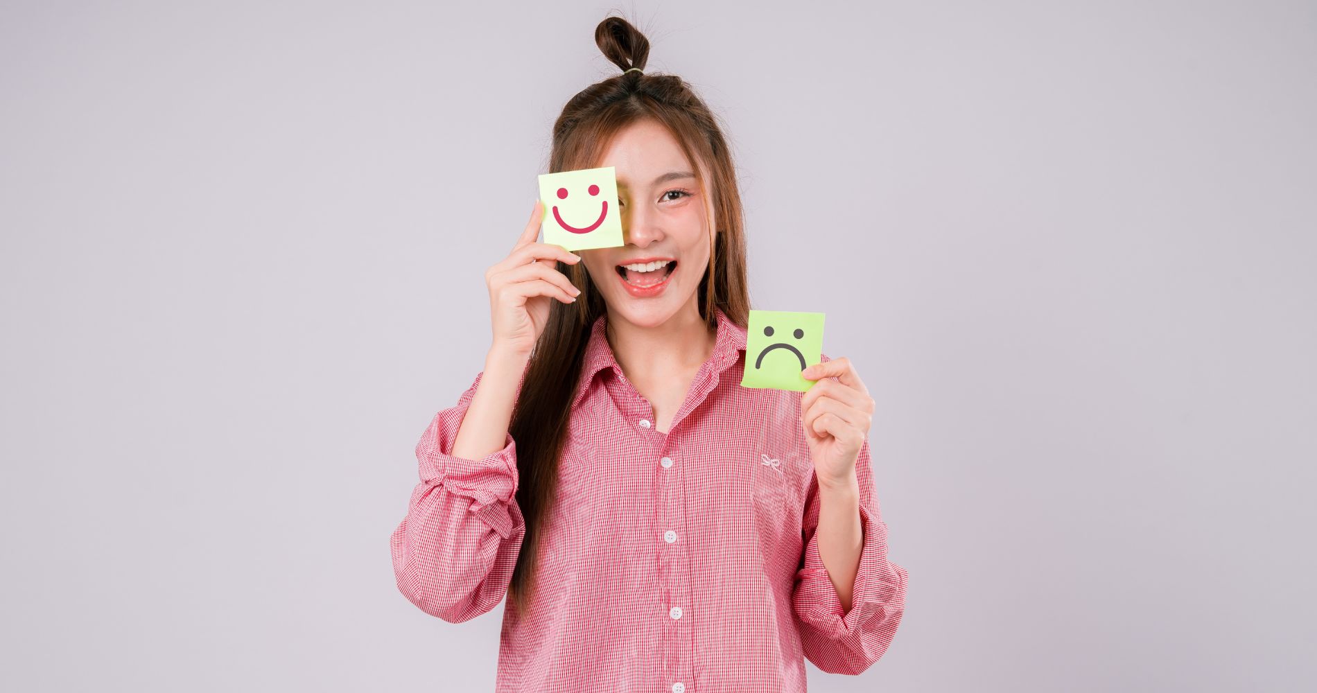 Kobieta trzymająca karteczki z uśmiechniętą i smutną buźką – symbol wpływu tryptofanu na nastrój i samopoczucie.